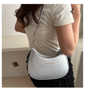 Side view of silver crescent underarm bag with gold logo and slim shoulder strap