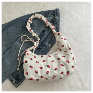 Detail of white corduroy shoulder bag with red strawberry embroidery and ruffled strap