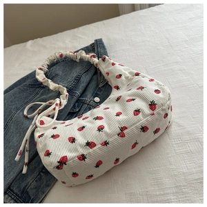 Detalle del bolso de pana con estampado de fresas y asas rizadas sobre fondo de mezclilla