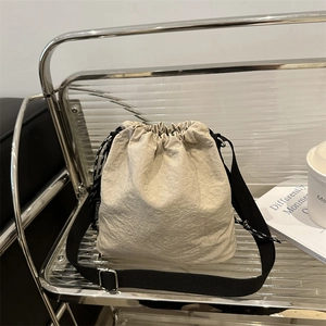 Beige lightweight drawstring bucket bag with black 'FASHION' strap on metal shelf