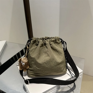 Olive green nylon drawstring bucket bag with adjustable strap and plush bear charm