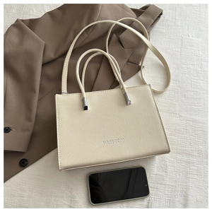 Detail of off-white lychee grain leather tote bag with FASHION logo and long strap
