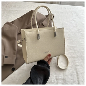 Detail of creamy white textured leather handbag with FASHION lettering on brown blazer