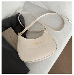 Détail d'un sac demi-lune crème avec logo doré posé sur une surface textile douce