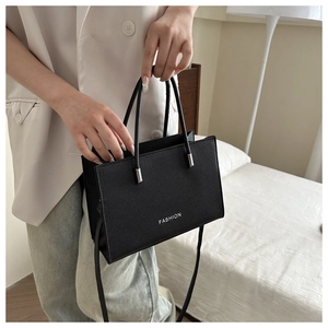 Close-up of black lychee-textured leather crossbody bag with white fashion logo lettering