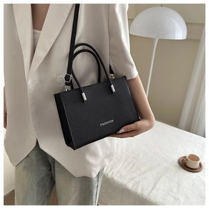 Crossbody black leather bag with FASHION text worn over a white suit jacket