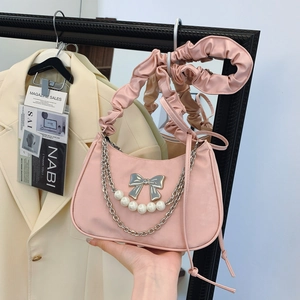 Pink pleated underarm bag with bow accent and pearl chain on cream suit background