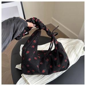 Detalle de bolso de hombro en pana negra con estampado de fresas y lazo decorativo en el asa