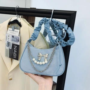 Blue pleated cloud bag with bow, pearls, and silver chains shown in lifestyle hand-held pose