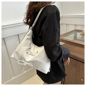 Detailed view of white bow shoulder bag with chain strap worn by a model in black shirt