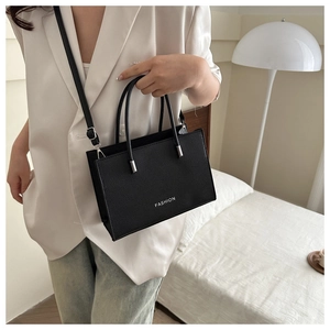 Detail of fashion square handbag in black lychee leather worn by a model in a suit