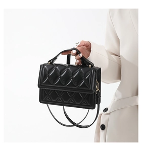 Detail of black quilted leather handbag worn with a chic cream-colored business suit