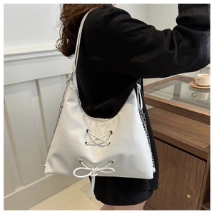 Detail of white Hobo bag with cross-lace design, bow ornament, and silver chain strap