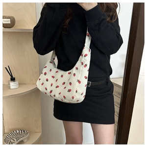 Detail of white corduroy shoulder bag with strawberry print on a model in a minimal setting
