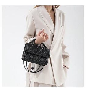 Detail of black quilted leather handbag with top handle and metal buckle on beige suit