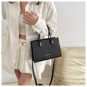 Detail of black crossbody bag with white FASHION text and litchi grain PU leather texture