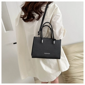 Detail of black pebbled leather tote bag with silver FASHION logo and adjustable strap