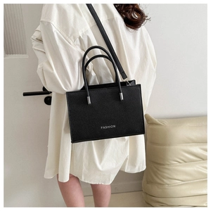 Minimalist black box handbag with FASHION lettering and litchi texture on a white dress