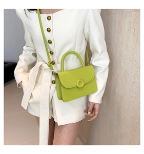 Close-up of fresh green mini crossbody bag with top handle and round metal buckle detail