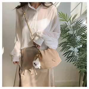 Détail du sac seau beige avec bandoulière en chaîne dorée et breloque ours en peluche