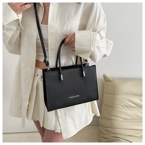 Close-up of black textured tote bag with FASHION lettering worn by a model in white