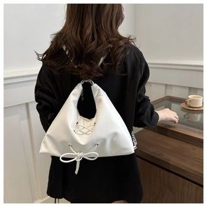 Detail view of a white triangular leather tote bag with lace-up bow and cross-strap design