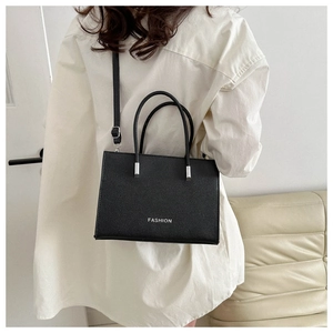 Detail of black pebbled leather tote bag featuring silver FASHION lettering and metal hardware