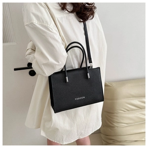 Detail of black pebbled leather handbag with silver FASHION logo worn by model