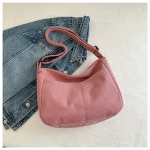 Close-up of pink corduroy crossbody bag with adjustable strap on denim jacket