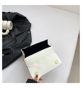 Detail view of white leather square crossbody bag with gold magnetic closures and black lining