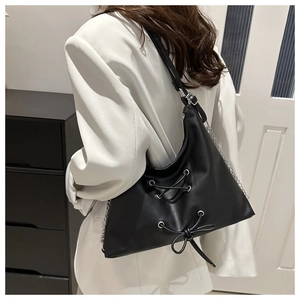 Detail of matte black bow hobo bag with lace-up design and metal chain strap on model
