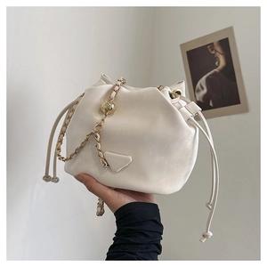 Detail van beige emmertas met trekkoord, gouden kettingriem en metalen fashion-plaatje