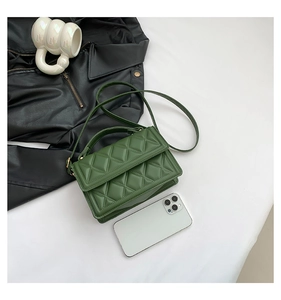 Flat lay of green quilted crossbody bag on white table with lifestyle accessories