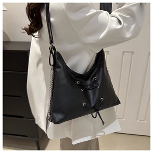 Detail of a black leather hobo bag featuring lace-up design and silver chain decoration