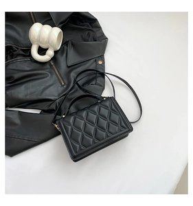 Detail of black quilted leather handbag with gold hardware and a long shoulder strap