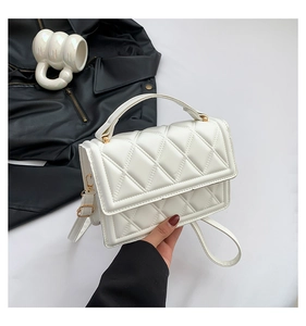 Detail of white quilted crossbody bag with top handle and gold hardware in stylish setup