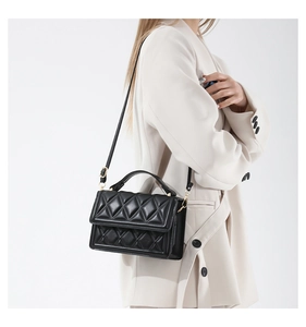Detail of black quilted leather shoulder bag with gold hardware and top handle strap