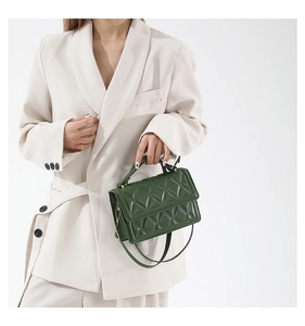 Detail of dark green quilted small square bag with top handle and gold hardware
