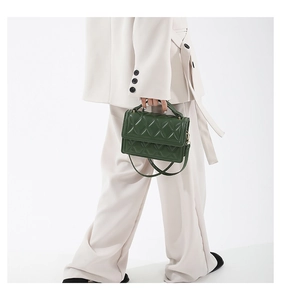 Detail of dark green quilted leather crossbody bag with metal chain and top handle