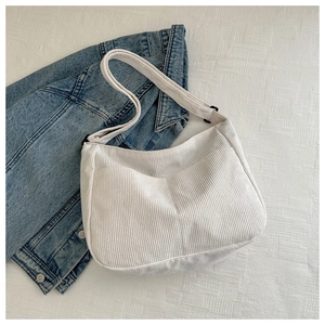 Detail of off-white corduroy hobo bag with adjustable strap over blue denim jacket