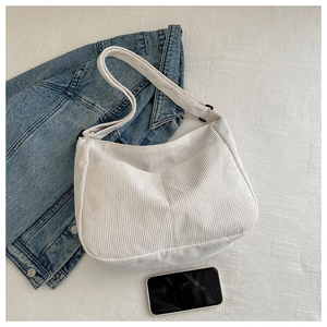 Flat lay of white corduroy crescent bag with adjustable strap and denim jacket
