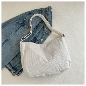 Close-up of white corduroy shoulder bag with wide adjustable strap on denim jacket