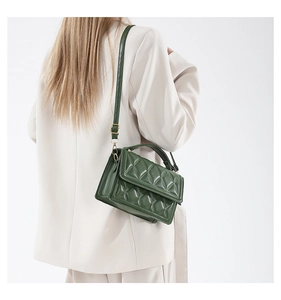 Detail of dark green quilted faux leather crossbody bag with gold hardware and strap