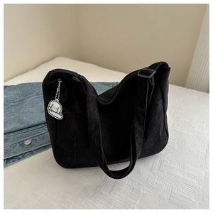 Detail of black corduroy shoulder bag with cloud charm and adjustable strap on white bed