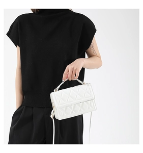 Detail of white quilted crossbody bag with textured rhombic pattern and top handle strap