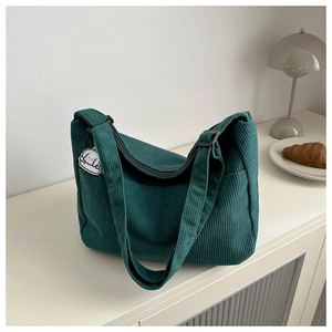 Detail of dark green corduroy shoulder bag with cute white puppy charm on the strap