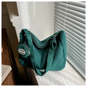 Detail of dark green corduroy shoulder bag showing texture and small matching pouch