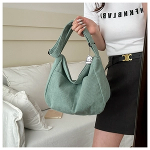 Detail of mint green corduroy hobo tote bag featuring a cute white plush puppy pendant
