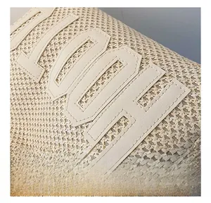 Close-up of woven straw texture and leather letter stitching on a beige tote bag