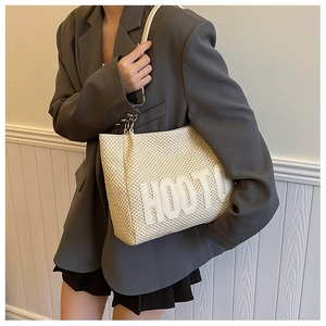 Detail of HOOTU embroidered letters on a large beige woven straw tote bag surface